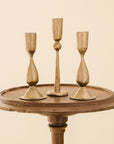 one tall and two short brass candlesticks on a wooden stool