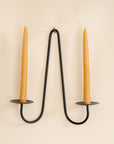 Black metal candle holder with two tan candles on a beige background