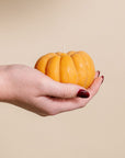 Hand holding a pumpkin-shaped candle against a beige background
