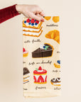 Dish towel with french dessert illustrations held by a person against a beige background
