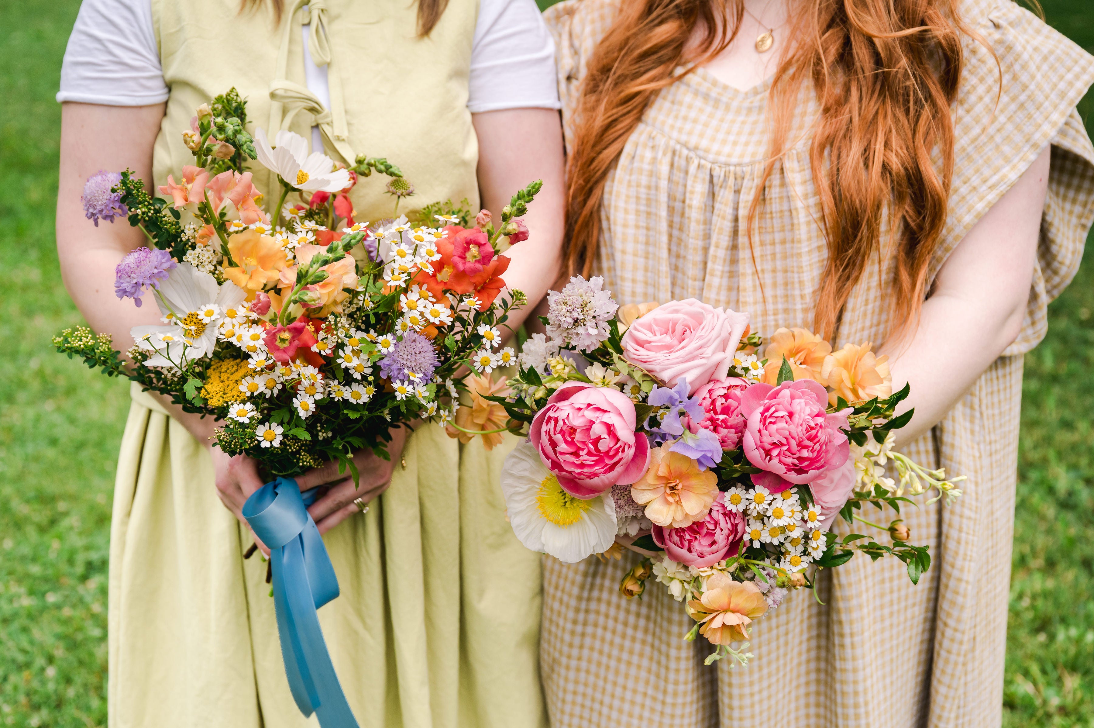 Two people holding colorful flower bouquets in a grassy outdoor setting