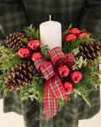 fragrant greenery, shiny red ball ornaments, red tartan, natural pinecones and a white pillar candle, held by a person in a green dress