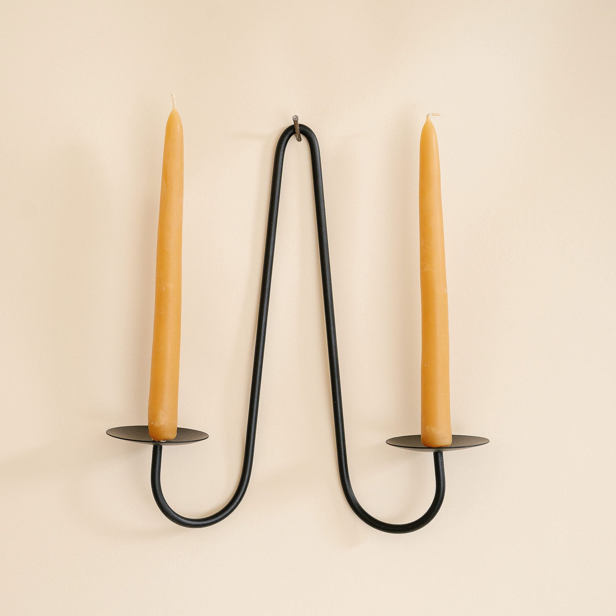 Black metal candle holder with two tan candles on a beige background