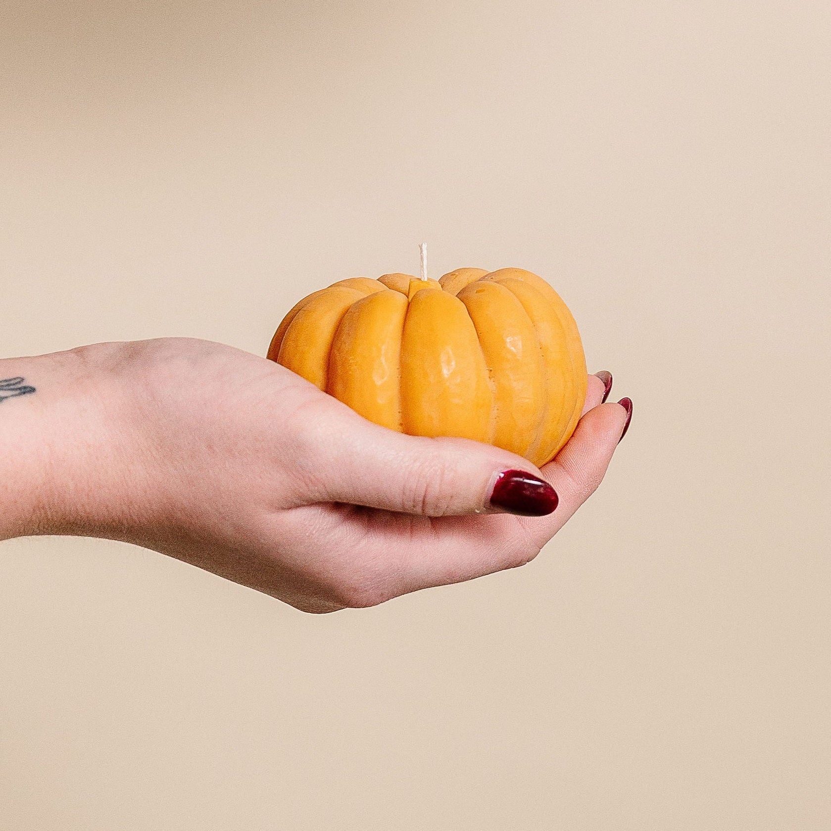 Hand holding a pumpkin-shaped candle against a beige background