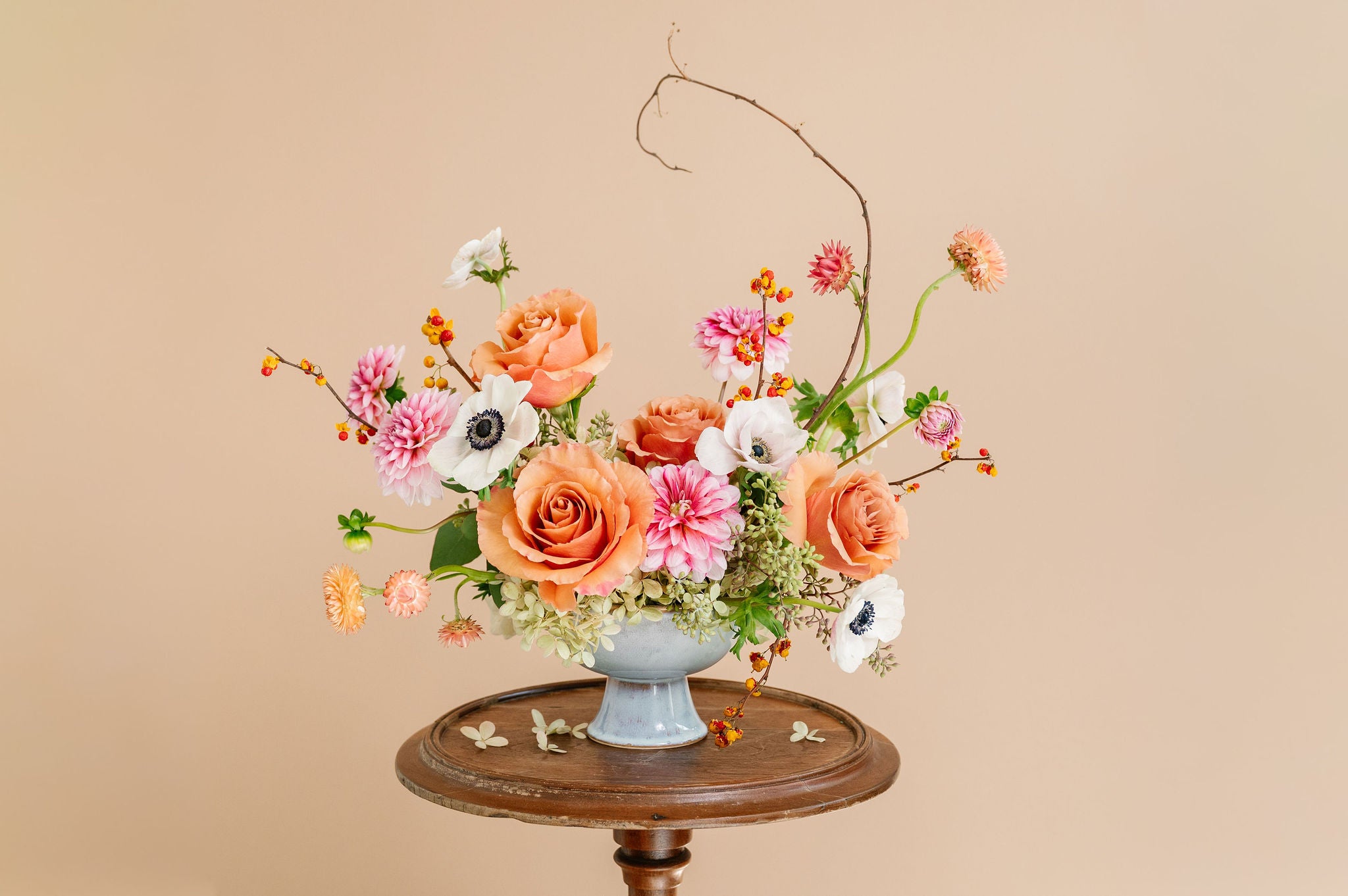 Floral arrangement in a white vase on a wooden table against a beige background