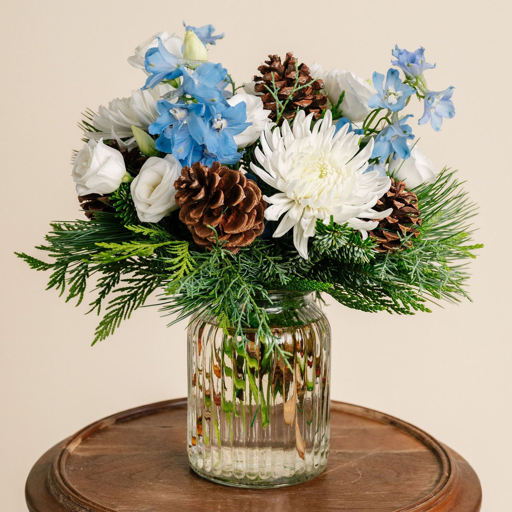 Glass vase with flowers and pinecones on a wooden table