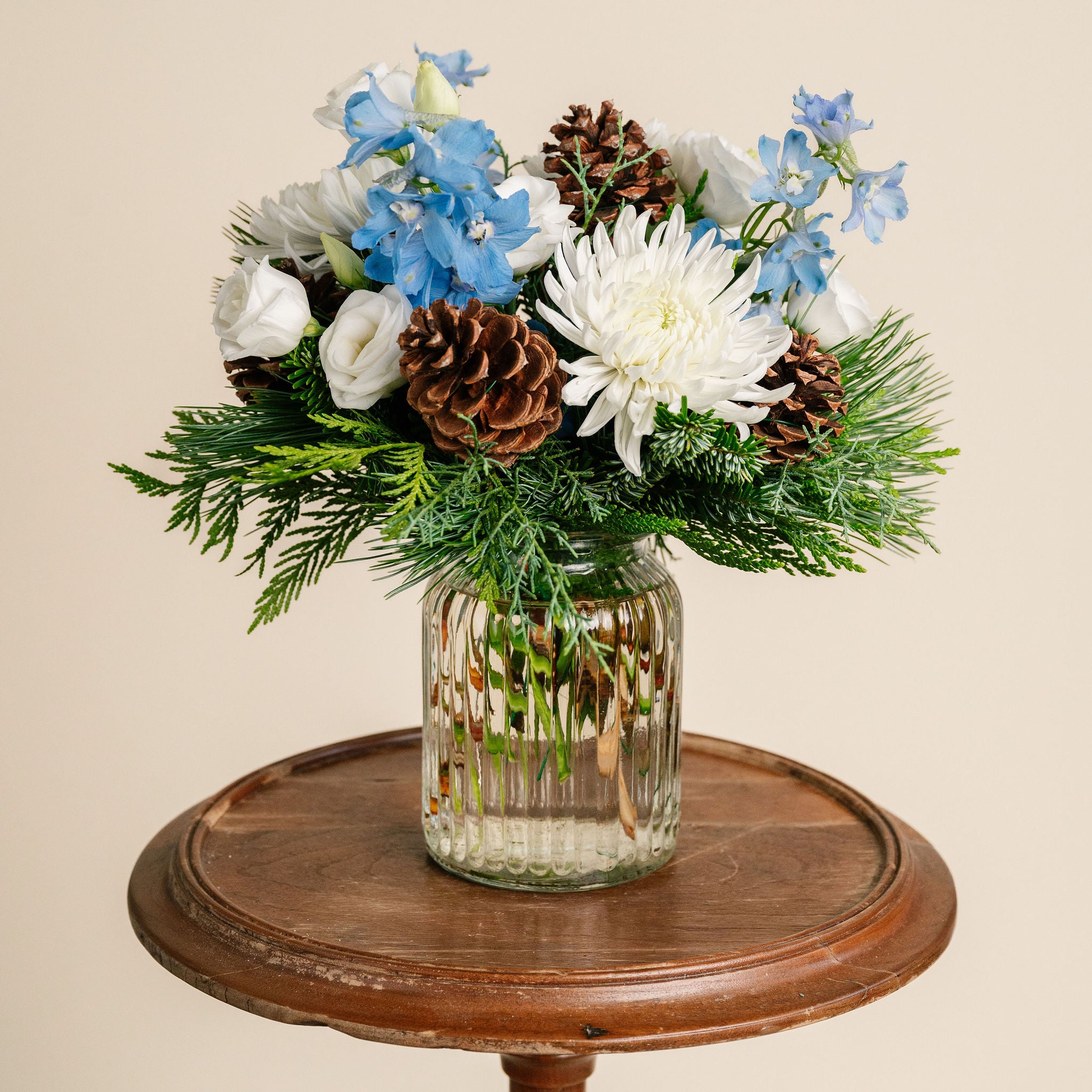 Glass vase with flowers and pinecones on a wooden table