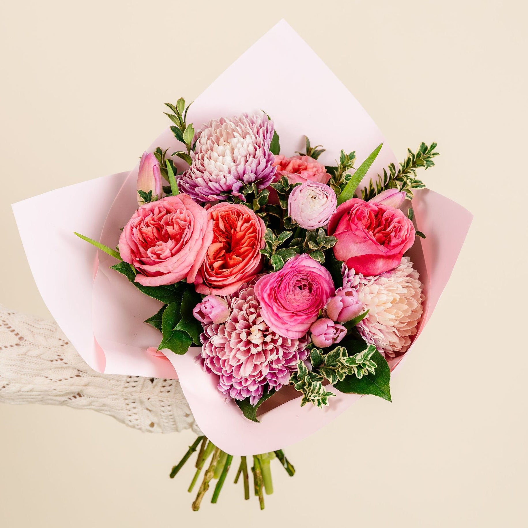 Bouquet of pink and white flowers with green leaves on a beige background