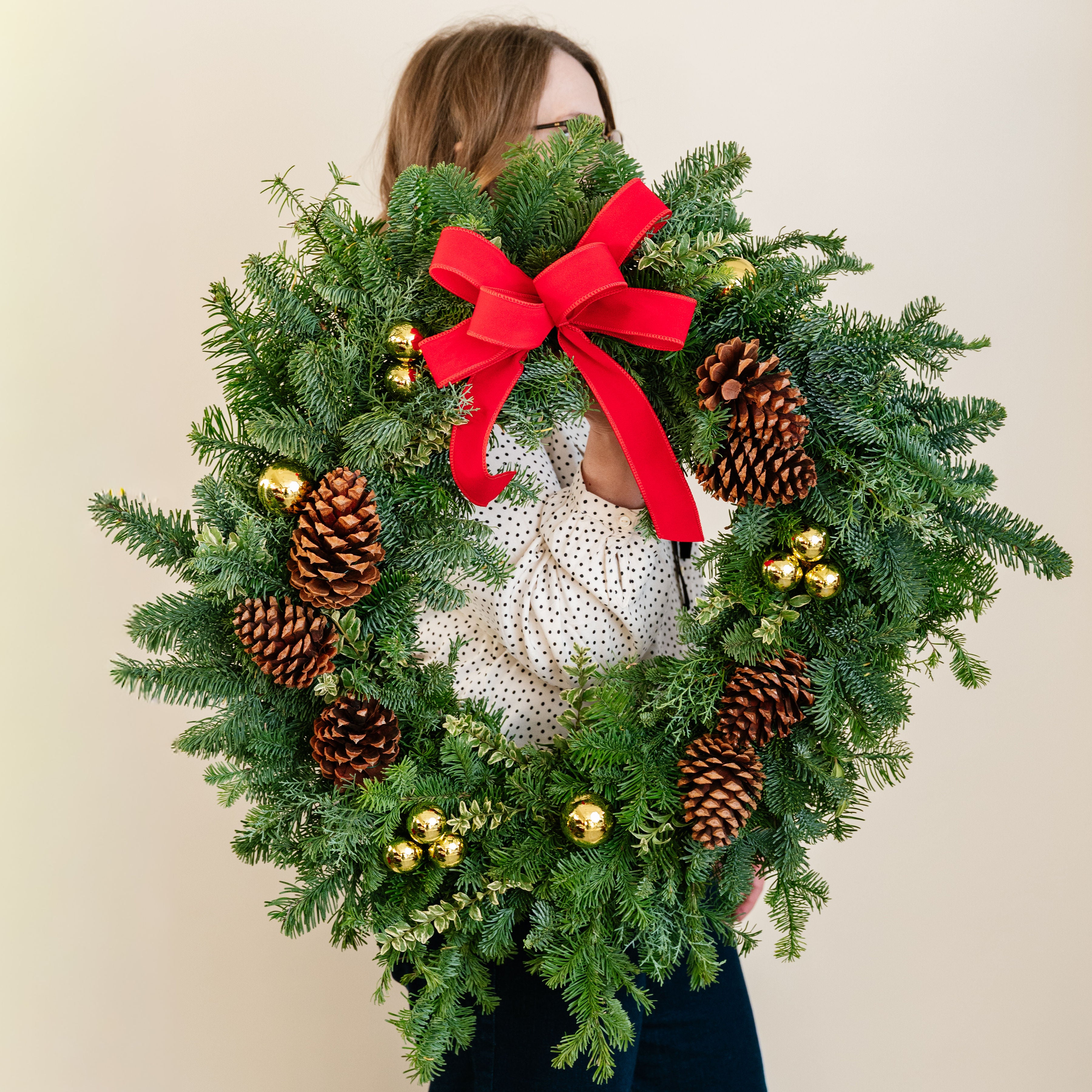 Person holding a Christmas wreath with a red bow and decorations against a plain background