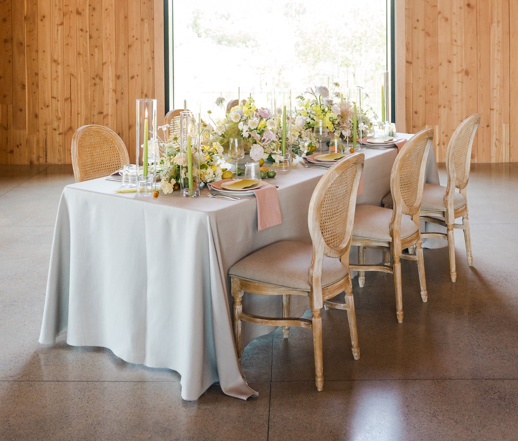 Dining table set with floral arrangements and candles in a room with wooden walls and large windows.