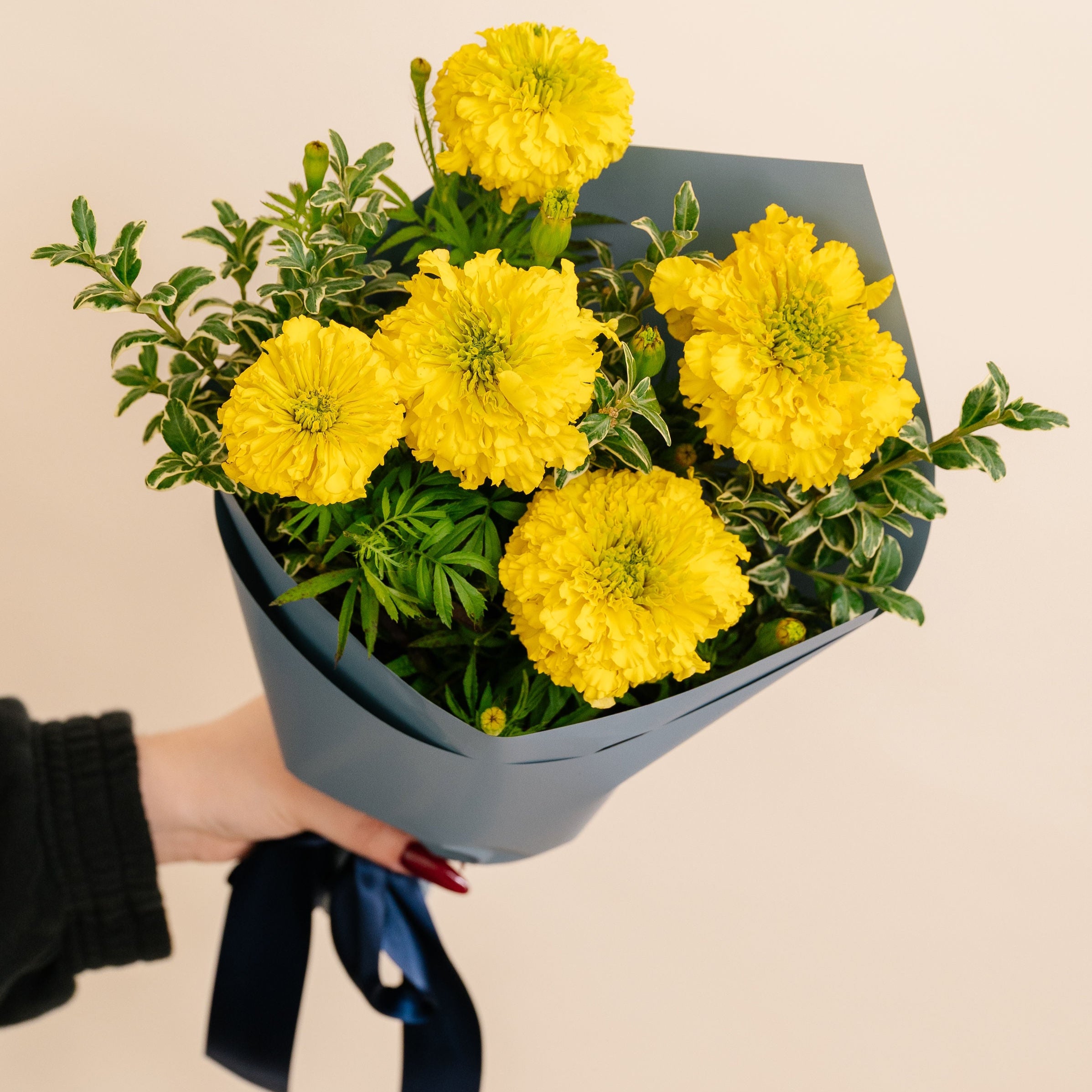 Bouquet of yellow flowers wrapped in gray paper held by a person against a beige background