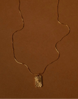 Gold necklace with a pendant on a brown background with 'Hunter & Bare' label.